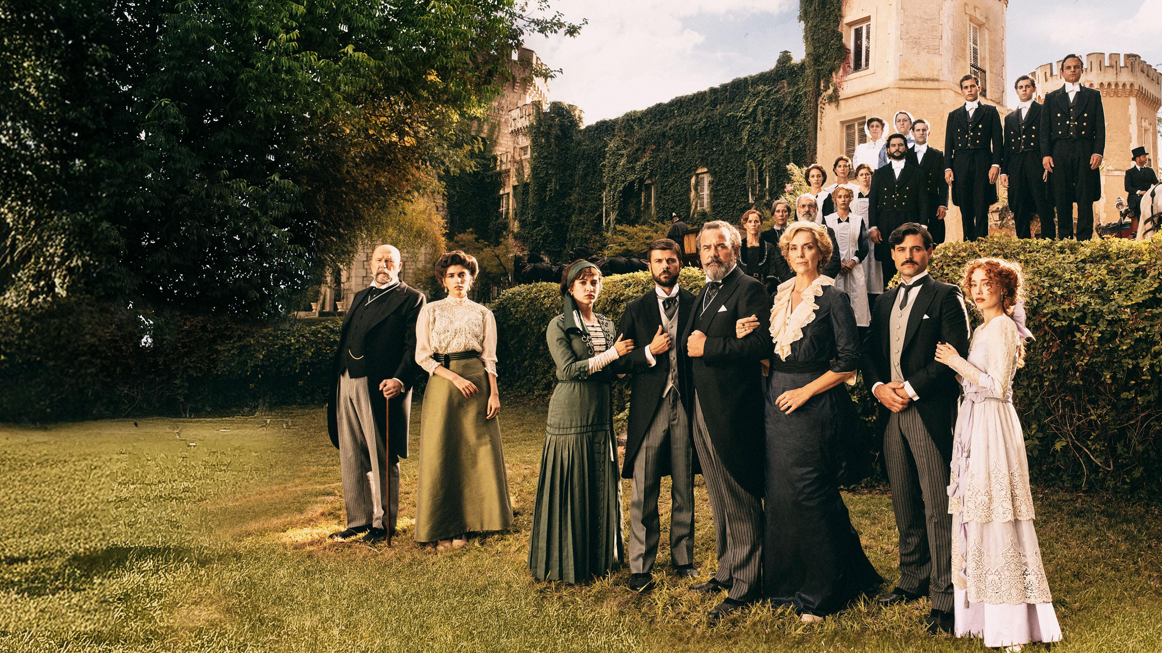Grupo numeroso de personajes vestidos de época posa en los jardines de un castillo cubierto de hiedra, en una escena coral de estilo histórico y cinematográfico.